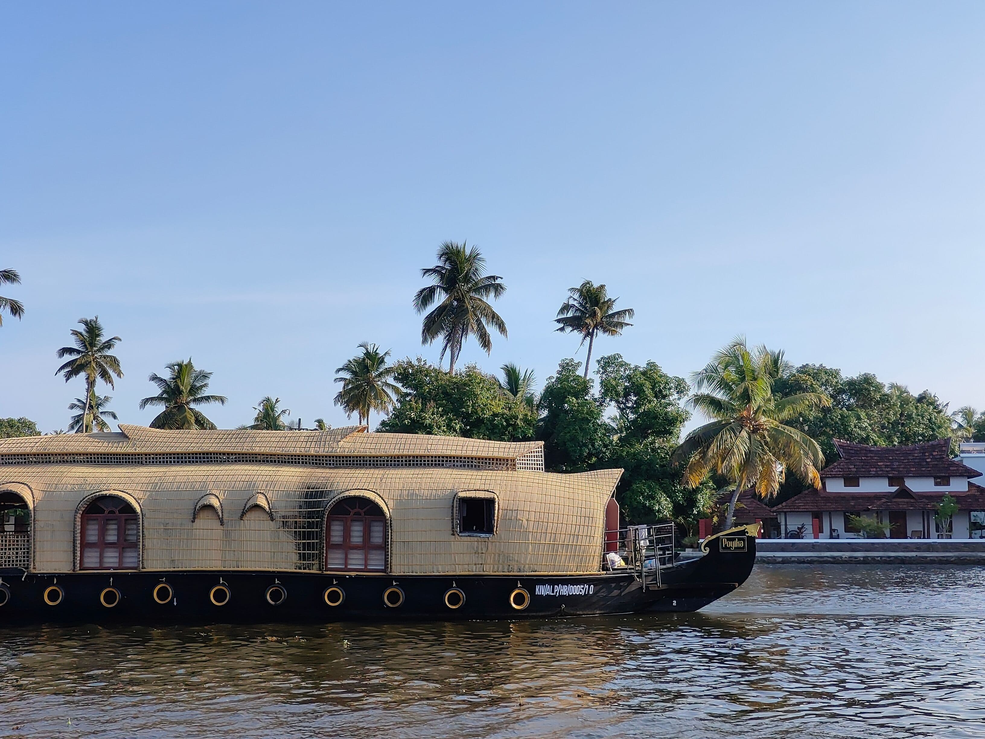 A serene view of a houseboat on the Kerala backwaters surrounded by palm trees.
